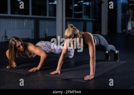 Female trainer teaches ward to do push-ups correctly. Beautiful woman trainer makes sure that her client, a young blonde, performs the exercises Stock Photo