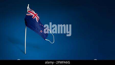 New Zealand mask on dark blue background. Waving flag of New Zealand painted on medical mask on pole. Virus Attack flag. Concept of The banner of the Stock Photo