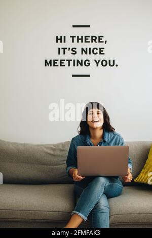 Positive female professional with laptop sitting at lobby. Cheerful businesswoman on sofa with laptop. Stock Photo
