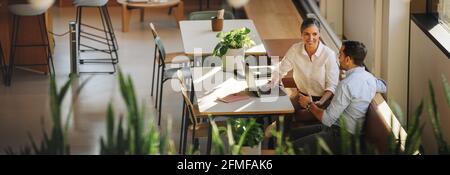 businesswoman with laptop explaining project details to colleague at office desk. business partners having meeting in coworking office space. Stock Photo