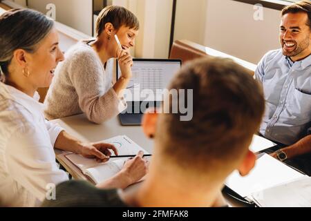 Smiling business people during review meeting sitting around table. Creative team looking happy in meeting. Stock Photo