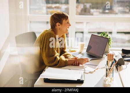 Smiling businessman sitting at her desk. Female executive looking away and smiling while working in office. Stock Photo