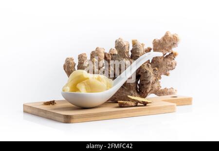 Ginger root and pickled ginger slices in a spoon, close-up. Cooking a ginger for sushi with bamboo cutting board on white background. Tradition spices Stock Photo