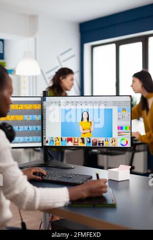 Black retoucher woman analysing images on pc with two monitors and retouching digital assets with stylus pencil. African project designer using photo editing software sitting in creative agency office Stock Photo