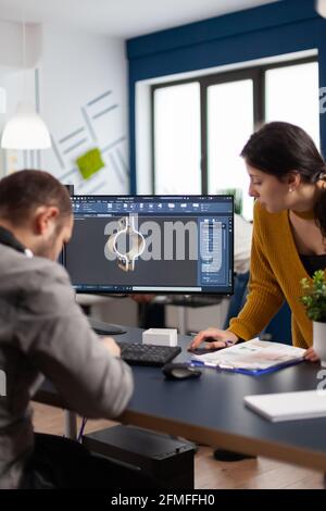 Coworkers engineer architects working on modern cad program developing construction metalic components. Industrial designer studying prototype idea on pc showing digital software with gears Stock Photo