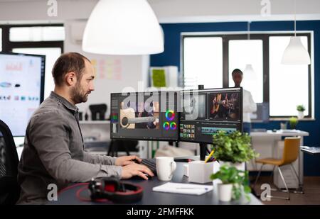 Video editor processing movie montage cutting footage and sound using post production software and two monitors. Man videographer editing film project in digital multimedia star up company Stock Photo