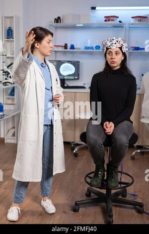 Scientist doing brain analysis using headset with sensors on patient explayning diagnosis. Monitor shows modern brain study. Wearing neuroscience headset analysis. Stock Photo