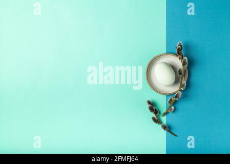 Top view of colored egg with willow branches on bicolor blue background. Minimalist flat lay. Space for text. Stock Photo