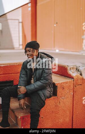 A handsome stylish Spanish man with a beanie posing while sitting on red stairs outdoors Stock Photo