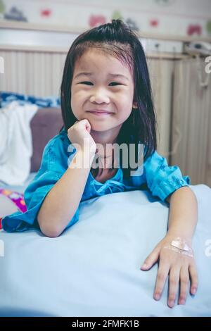Illness asian child smiling happily and looking at camera. Young pretty girl admitted in hospital while band-aid on hand. Health care stories. Vintage Stock Photo