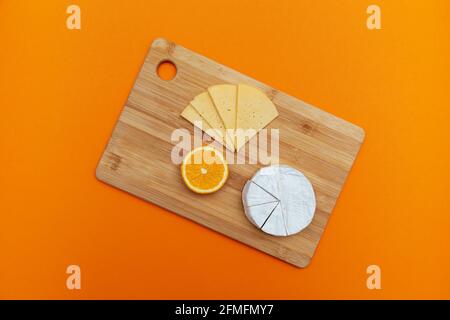 Wooden board with different cheeses and orange on a ginger background. Top view, flat layout. Stock Photo