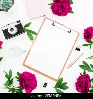 Home office composition. Freelancer workspace with clipboard, diary, retro film camera, flowers and accessories on white. Flat lay, top view. Stock Photo