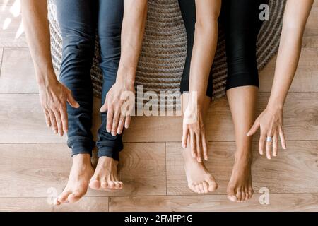 Close up of barefoot couple sitting and warming up in sportswear on the floor at home before online work. Young man and woman stretching their arms Stock Photo