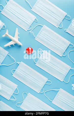 A toy white airplane and protective masks on a blue background with a red dot as the destination. The concept of a ban on flights and a mask mode, the Stock Photo