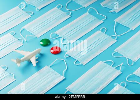 A white plane surrounded by protective masks on a blue background with a green and red dot as the destination. The concept of allowing and banning air Stock Photo