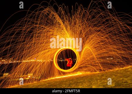 Large round burning fireworks sparkle from the burning steel wool. The city lights at night. Stock Photo