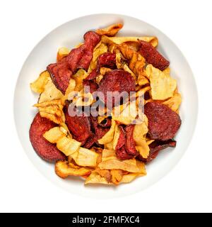 Mixed root vegetable crisps, in a white bowl. Mix of sliced root vegetables, parsnips, beetroots and carrots, fried in sunflower oil, with sea salt. Stock Photo