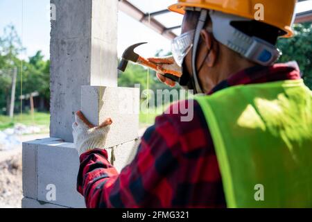 Close-up of bricklayer builder use a hammer to help with autoclaved aerated concrete blocks. Walling, installing bricks on construction site Stock Photo
