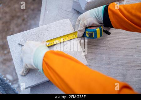 Close-up hand of The tiler used a tape measure to measure the size of the lightweight bricks on the construction site. Stock Photo