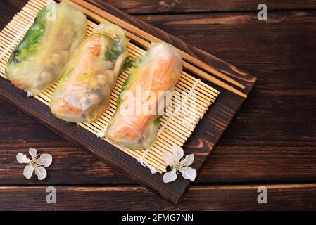 Fresh three spring rolls with cherry flowers on wooden board, vietnamese, asian food, close up. Stock Photo