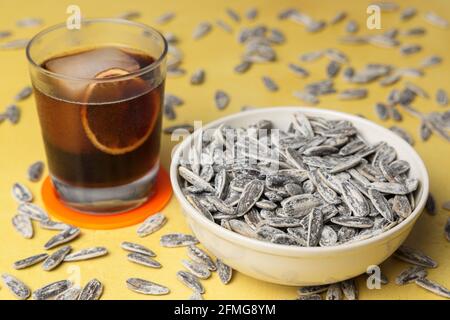 Pile of salted sunflower seeds in a bowl and a cold drink on a yellow background Stock Photo