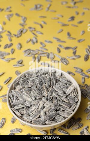Pile of salted and roasted sunflower seeds in a bowl on a yellow background Stock Photo