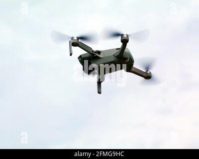 Isolated small drone with camera hovering in the air. blue and gray clear sky. closeup view. whirling and fast rotating propellers. aerial photography Stock Photo