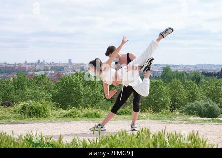 Young couple practicing street dance, ballet, dancing steps, movements at a park wearing protective face masks. Stock Photo