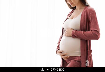 Motherhood Concept. Cropped Image Of Young Pregnant Woman Tenderly Embracing Her Tummy Stock Photo