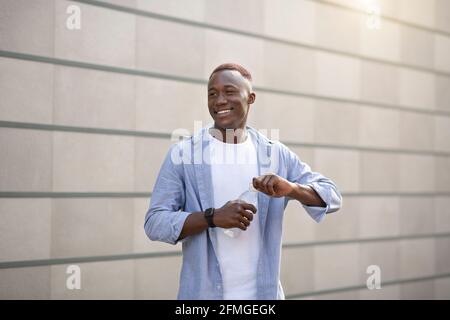 Keep hydrated. Happy African American guy with bottle of fresh mineral water near brick wall at city Stock Photo