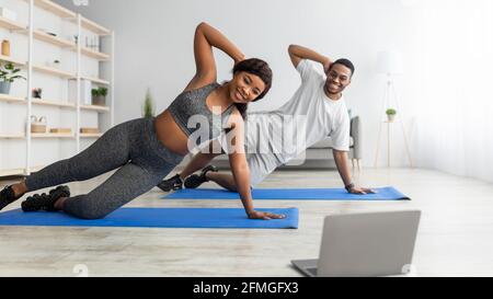 Online sports during covid lockdown. Fit black couple doing exercises in front of laptop at home, copy space Stock Photo