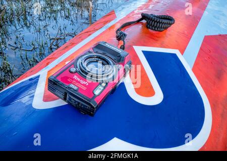 Fort Collins, CO, USA - May 4, 2021: Compact, waterproof Olympus Stylus Tough TG-5 camera on a wet deck of a stand up paddleboard by Mistral