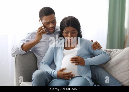 Worried black man calling doctor while wife having labor pains Stock Photo