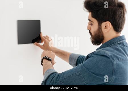 Arab guy using thermostat smart home domotic control panel on wall for house temperature Stock Photo