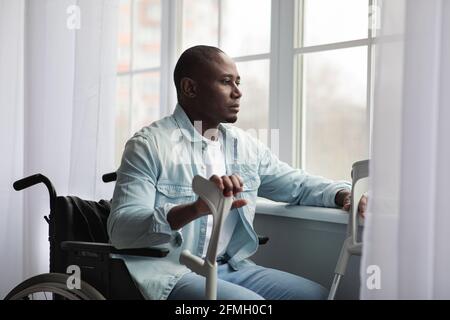 Sad disabled mature african american man in wheelchair sits in front of large window Stock Photo