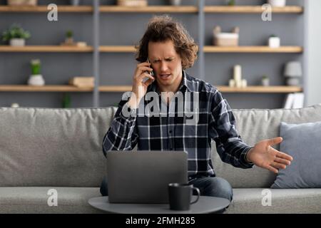 Discontented Man Talking On Phone Having Problem At Home Stock Photo