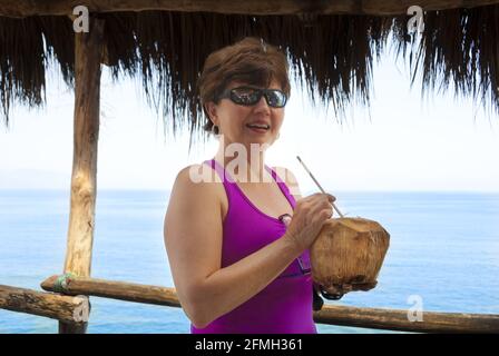 Woman drinking fresh coconut juice through straw at palapa kiosk on the Bay of Banderas, Puerto Vallarta on the Pacific coast of Mexico Stock Photo