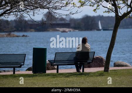 Helsinki / Finland - MAY 9, 2021: A woman sitting on a bench in the public park looking at the sea. Stock Photo