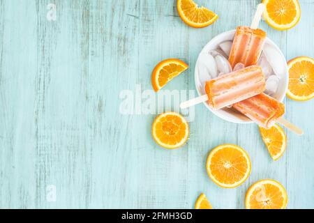 Tangerine popsicles in a bowl of ice with sliced oranges summer picnic food on blue wood backdrop table Stock Photo
