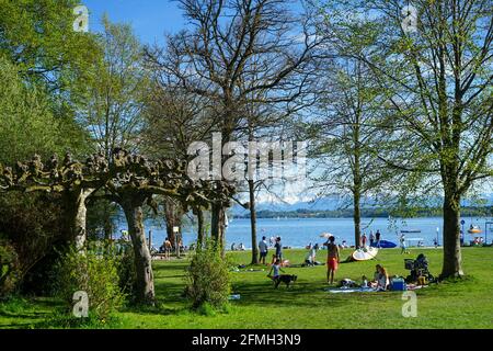 Numerous people enjoy their leisure time in the sunshine on the shore of a lake. Stock Photo