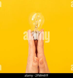 Concept of the new idea, light bulb in hand close-up on orange yellow background, isolated photo Stock Photo