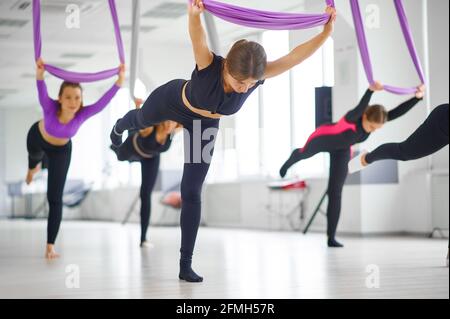 Full body of fit female in sportswear practicing aerial yoga on