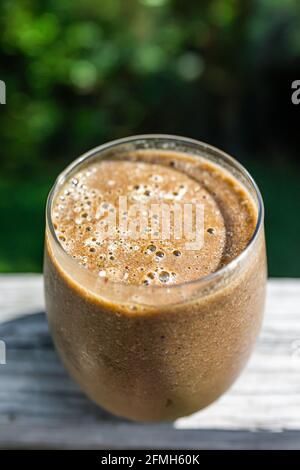Closeup of green vegetable fruit smoothie in glass outside outdoors on wooden deck fence as healthy raw vegan breakfast with background of sunny summe Stock Photo