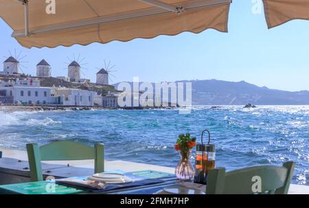 Mykonos, panoramic view of white famous windmills  Chairs with tables in typical Greek restaurant  of Little Venice in Cyclades island, Greece. Stock Photo