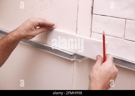 Stylish trendy white ceramic tiles on the kitchen wall. Hands in the process of laying white rectangular tiles on the bathroom wall. Renovation of apa Stock Photo