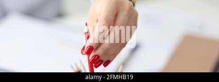 Female hand with red manicure pulling out pencil in office closeup Stock Photo