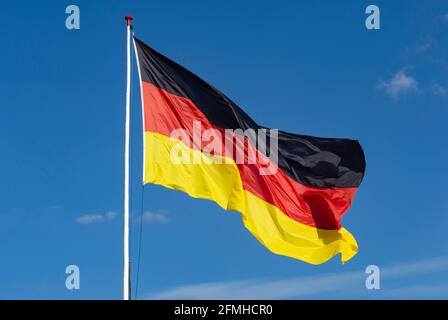 big German Flag flying from handmade wooden flag pole with white paint  with a cloudless blue sky behind it Stock Photo