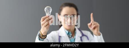 Woman doctor holding light bulb in hands and showing index finger up Stock Photo