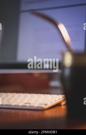 A vertical shot of a wireless keyboard on the table with a computer and a drink on it Stock Photo
