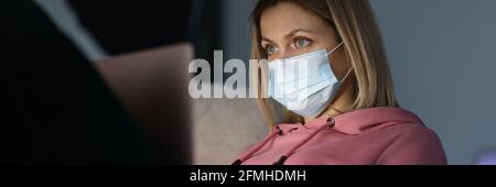 Young woman in protective medical mask sitting in front of laptop at home Stock Photo